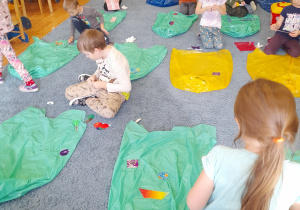 Dzieci na dywanie ozdabiają worki na śmieci kolorowymi wzorami z folii samoprzylepnej.