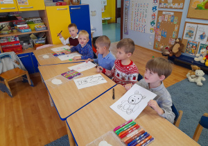 Grupa dzieci przy stolikach rysuje misia w oparciu o film instruktażowy.