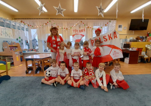 Zdjęcie grupowe dzieci i nauczycielki w strojach biało – czerwonych.