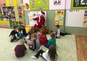 Dzieci siedzą na dywanie Mikołaj czyta świąteczne opowiadanie.