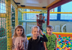 Czworo dzieci na tle basenu z piłkami i sprzętu w sali zabaw