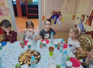 Dzieci siedzą przy stoliku, degustują przygotowane słodycze.