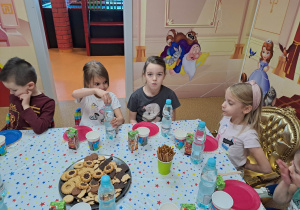 Dzieci siedzą przy stoliku, degustują przygotowane słodycze.