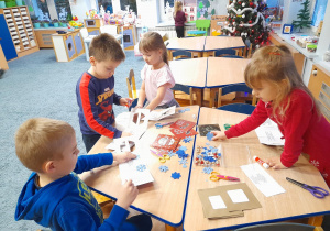 Dzieci przy stolikach przygotowują kartki z życzeniami.