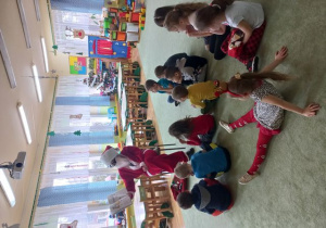 Dzieci siedzą na dywanie i słuchają opowiadania czytanego przez Mikołaja