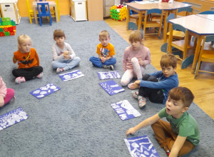 Dzieci ze swoimi pracami siedzą na dywanie i omawiają swoją pracę.