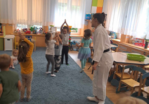 Dzieci ćwiczą na dywanie pod okiem trenerki karate.