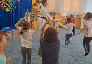Dzieci ćwiczą na dywanie pod okiem trenerki karate.