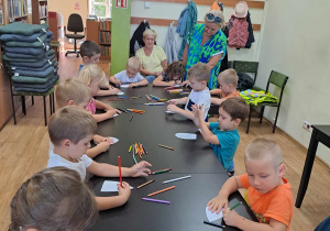 Dzieci przy długim stole kolorują kredkami listki drzewa.