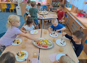 Grupa dzieci przy stolikach wykonuje sałatkę owocową.