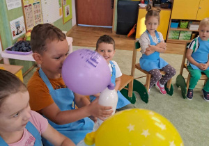 Dzieci dmuchają balony przy pomocy butelek.
