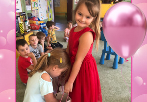 Fotografia w kolorowej, urodzinowej ramce - dziewczynka w czerwonej sukience częstuje dzieci cukierkami.