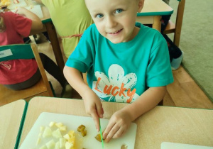 Chłopiec siedzi przy stoliku i kroi owoce na sałatkę