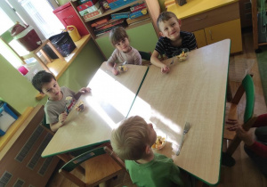 Czworo dzieci spożywa sałatkę owocową siedząc przy stoliku