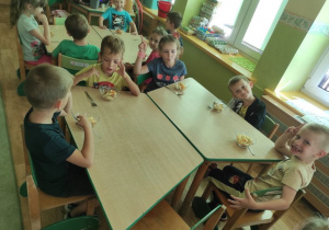 Grupa dzieci siedzi przy stoliku i wesoło pozuje mając przed sobą salaterki z własnoręcznie wykonaną sałatką owocową