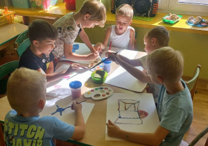 Dzieci siedzą przy stoliku, malują farbami