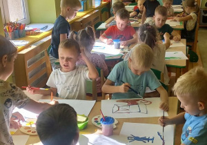 Grupa dzieci przy stolikach maluje farbami