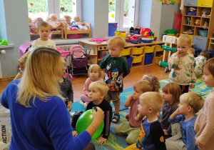 Pani logopedka prezentuje dzieciom ćwiczenie z balonikiem.
