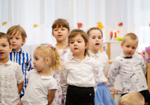 Przedszkolaki w galowych strojach stoją podczas występu.
