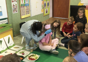 Nauczycielka częstuje uczennicę warzywem.