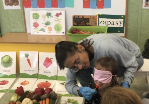 Nauczycielka częstuje uczennicę warzywem.