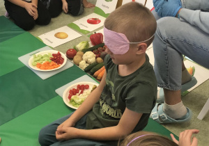Chłopiec smakuje warzywo z zamkniętymi oczami.