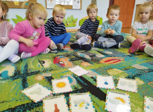 Dzieci siedzące na dywanie oglądające obrazki związane z pogodą.