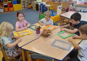 Dzieci siedząc przy stolikach tworząc kompozycję z misiem Uszatkiem.