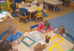 Dzieci siedząc przy stolikach tworząc kompozycję z misiem Uszatkiem