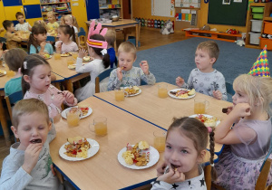 Dzieci przy stolikach zajadają się słodkościami.