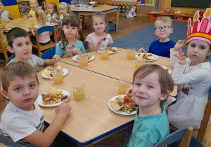 Dzieci przy stolikach zajadają się słodkościami.