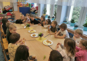 Grupa dzieci przy stolikach podczas słodkiego poczęstunku.