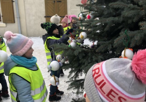 Dzieci z grupy IV ozdabiają świąteczne drzewko bombkami w kształcie bałwanków.