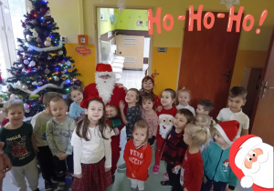 Dzieci stoją z Mikołajem w korytarzu przedszkola.