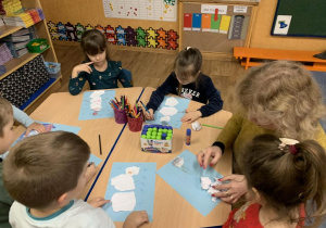 Dzieci przy stoliku przyklejają wydarte z papieru kawałki papieru tworząc bałwanka