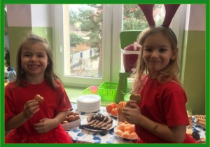 Dwie dziewczynki przebrane za renifery kosztują słodyczy na tle stołu.