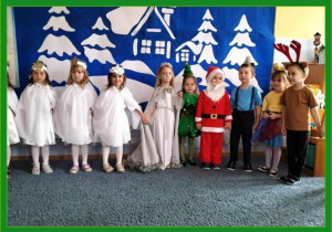 Dzieci w świątecznych przebraniach stoją na świątecznym tle.