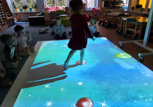 Dziewczynka podczas zabawy na Magicznym Dywanie, obserwowana przez inne dzieci.