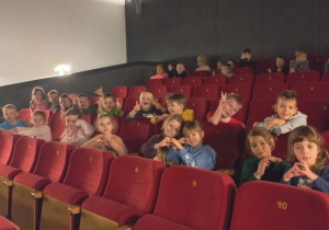 Dzieci siedzą w kinowych fotelach czekając na seans filmowy