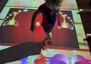 Dziewczynka w stroju gimnastycznym podczas zabaw na interaktywnej macie.