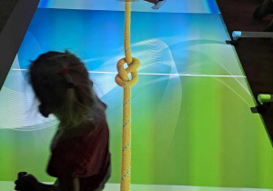 Dwoje dzieci bawi się w przeciąganie liny na interaktywnym dywanie.