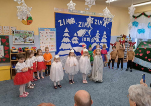 Dzieci w różnych strojach podczas występu dla babć i dziadków, na pierwszym planie cztery dziewczynki przebrane za śnieżynki.