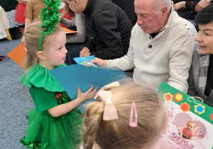 Mała dziewczynka w stroju choinki wręcza dziadkowi upominek - kalendarz.