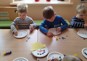 Dzieci przy stoliku wykonują bałwanki z talerzyków papierowych.
