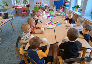 Dzieci siedzące przy stoliku i trzymające styropianowe kule w rączkach.