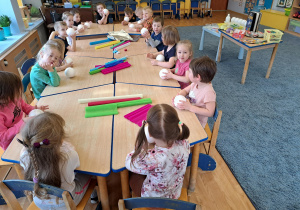 Dzieci siedzące przy stoliku i trzymające styropianowe kule w rączkach.