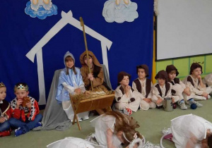 Dziewczynki-aniołki siedzą w kołach hula-hop na dywanie, w tle dzieci grające postacie Maryi i Józefa