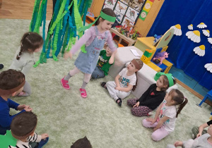 Dzieci w strojach dinozaurów podczas zabawy na dywanie.