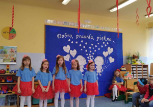 Grupa dziewczynek ubrana na czerwono-niebieski podczas śpiewania piosenki konkursowej.