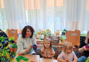 Dziewczynka wraz ze swoją mamą wspólnie tworzą palemkę z kolorowej bibuły.
